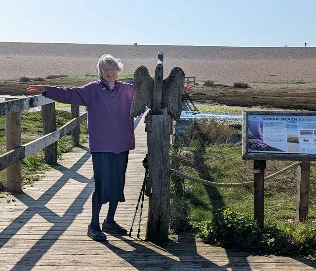 A client on a wooden boardwalk by the coast, arms stretched out, smiling